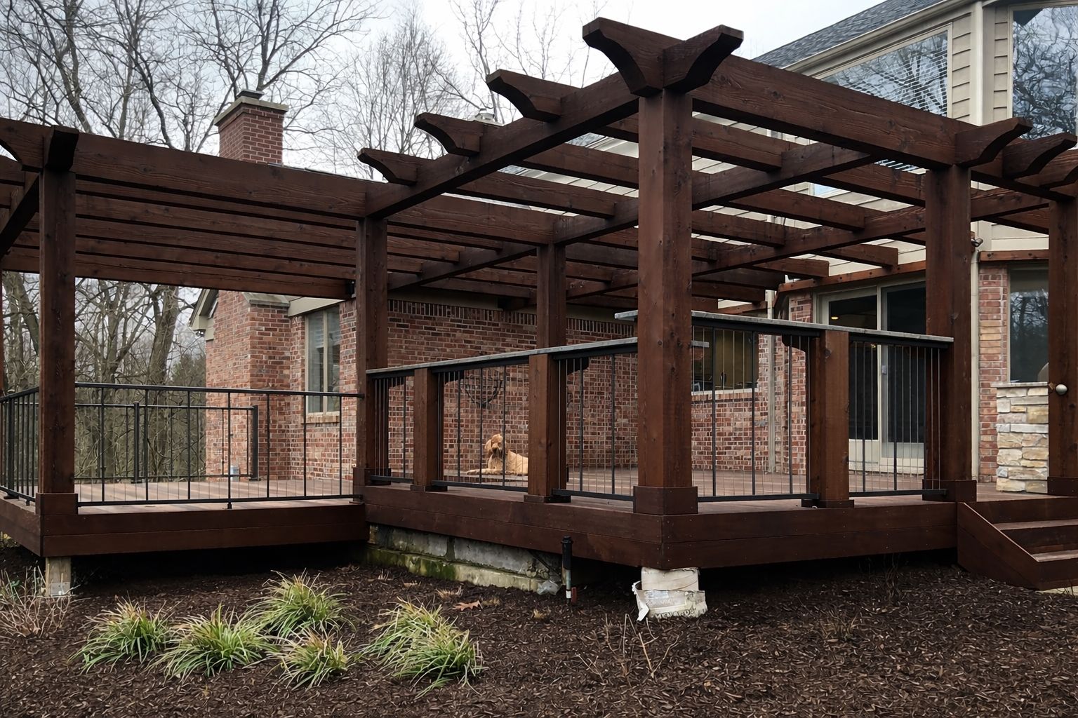 Wooden pergola over a raised deck attached to a brick and stone house.