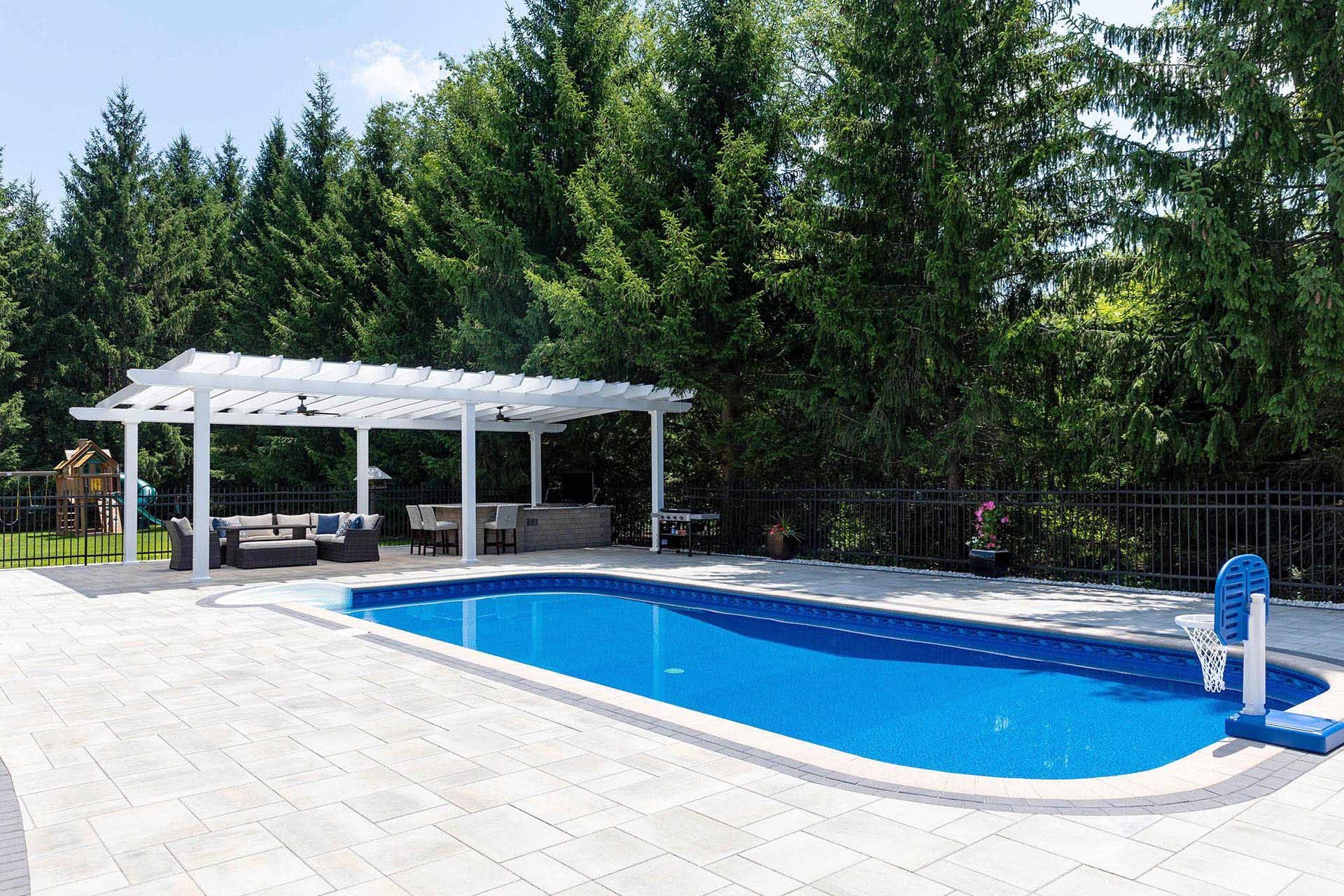 A blue swimming pool with a stone patio, next to a white pergola