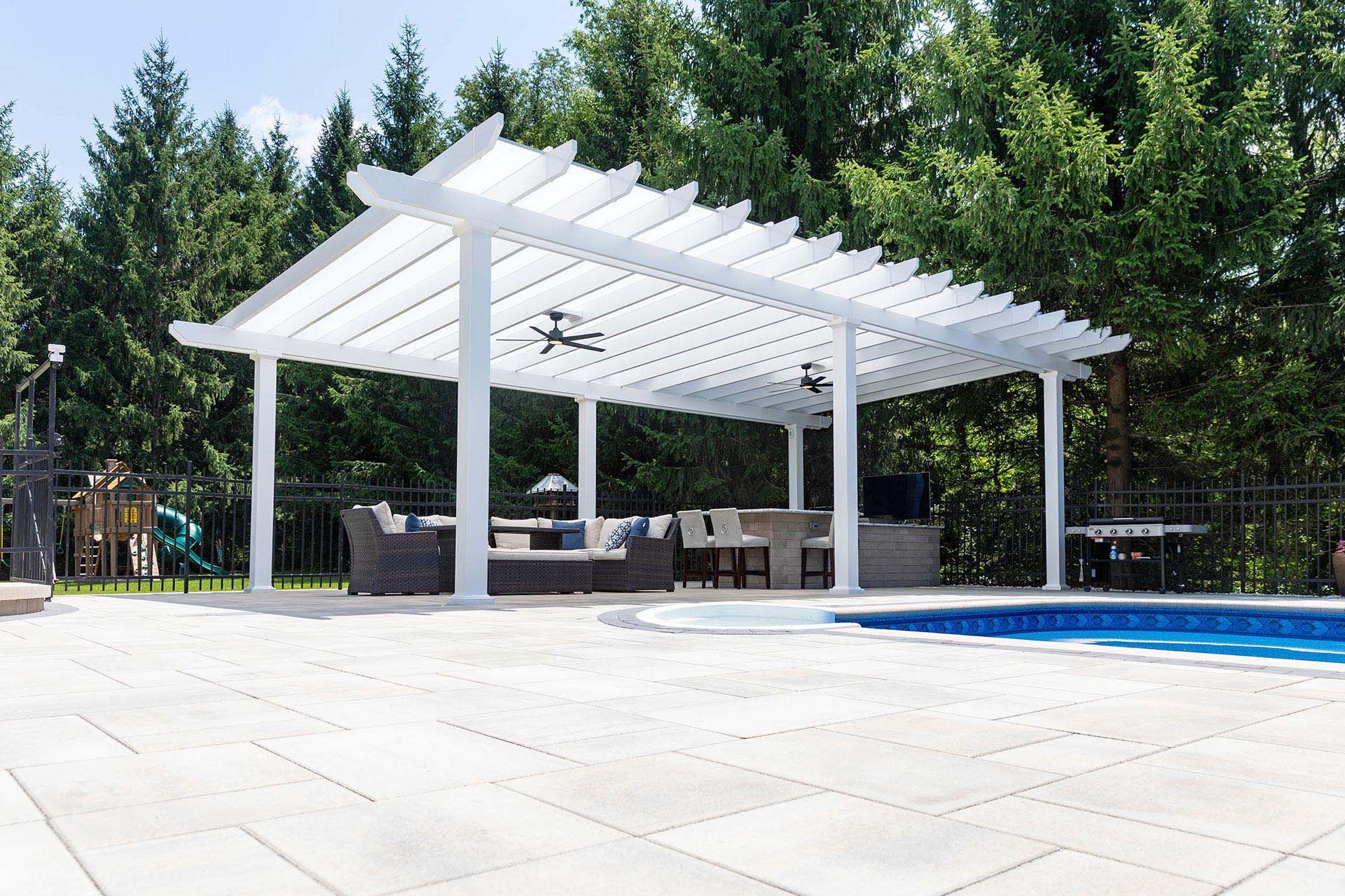 A white pergola with ceiling fans covers outdoor seating beside a swimming pool