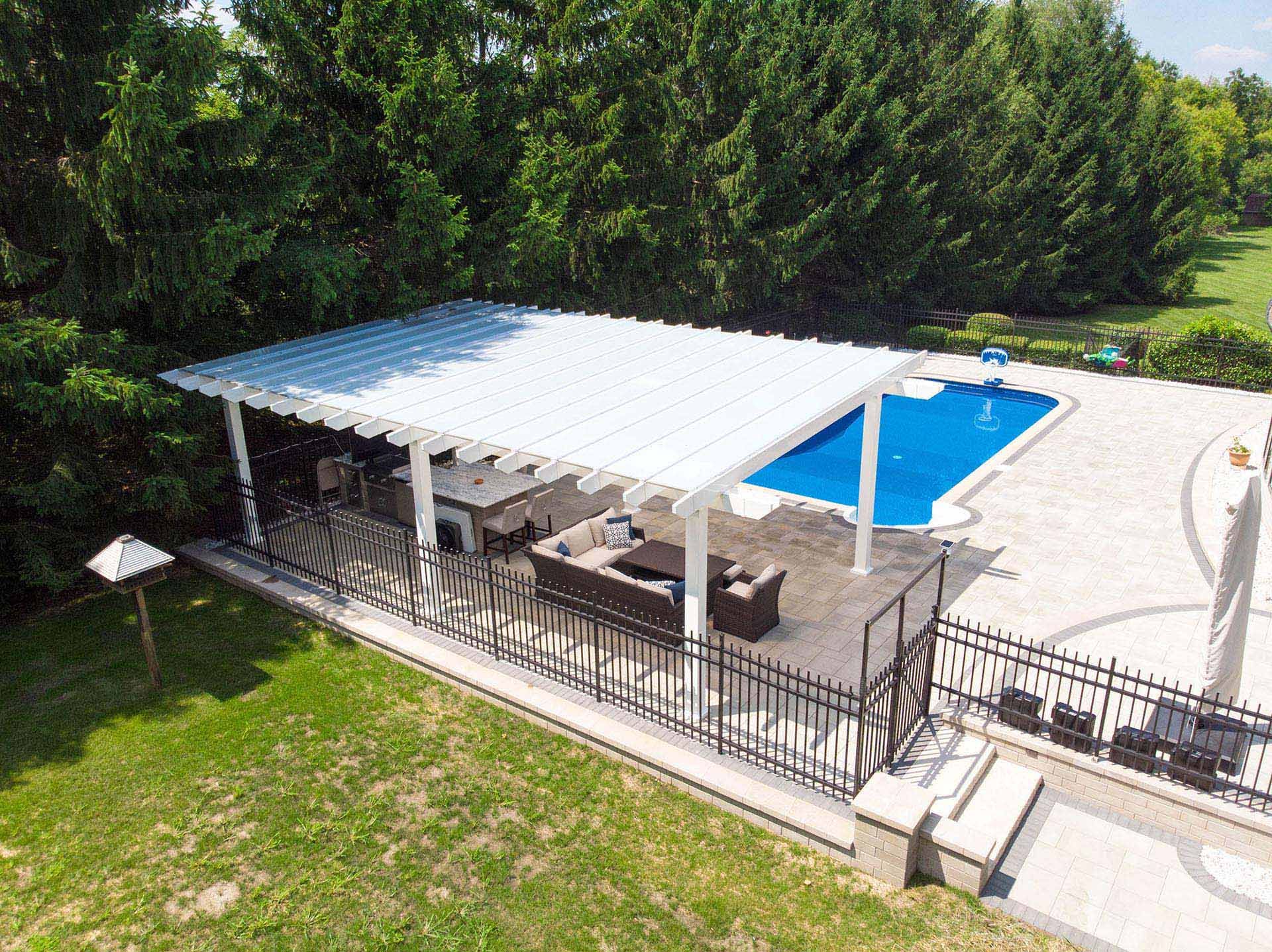 An aerial view of a white pergola covering a patio seating area next to a backyard swimming pool