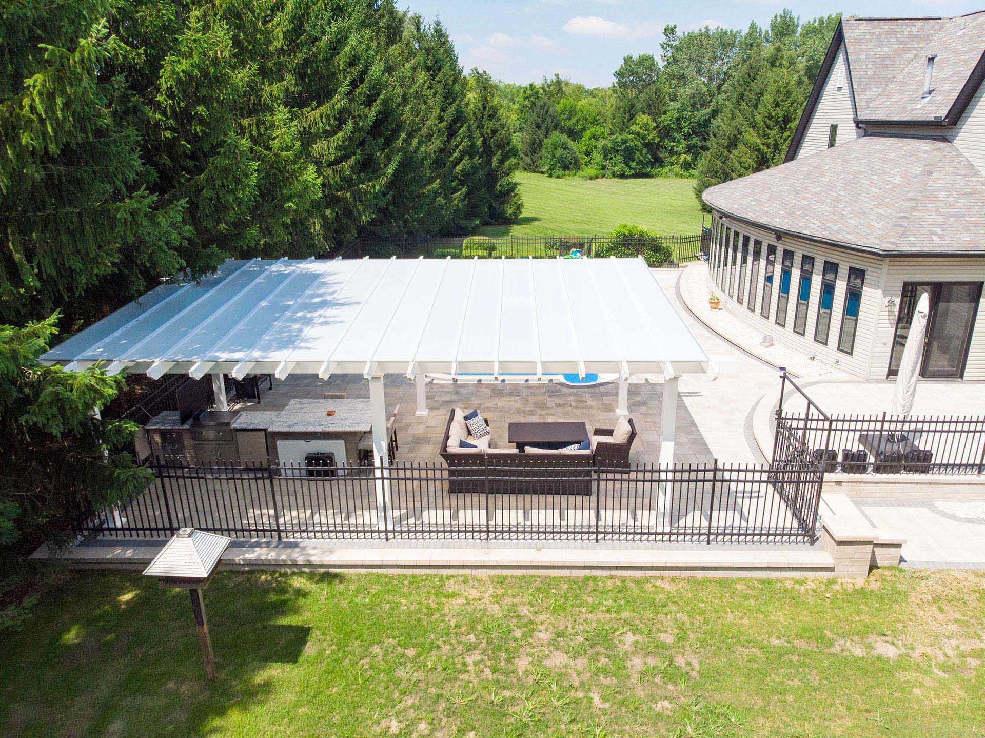 Aerial view of a white pergola-covered patio with outdoor seating and a kitchen next to a house