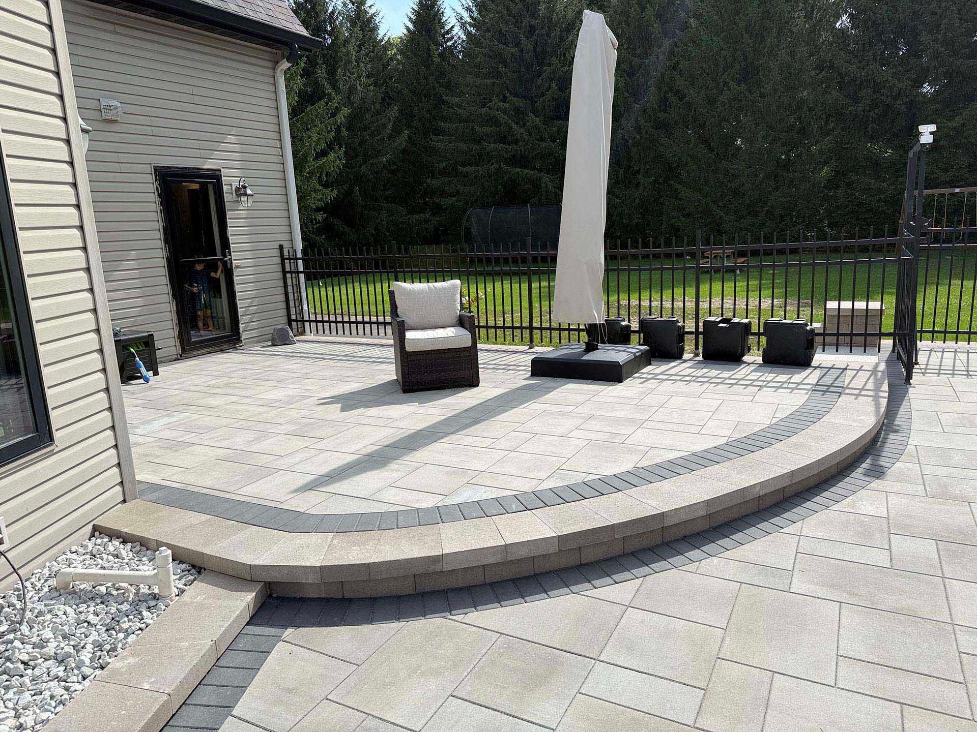 A paved patio with a curved stone retaining wall sits outside a house