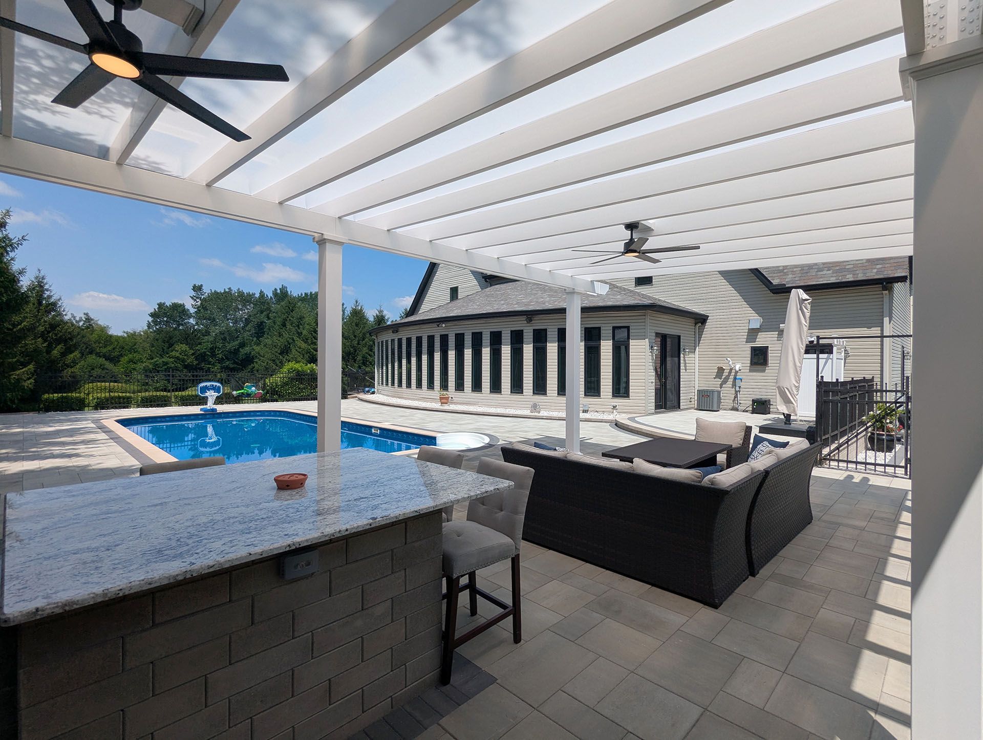 An outdoor kitchen and patio under a white pergola with ceiling fans