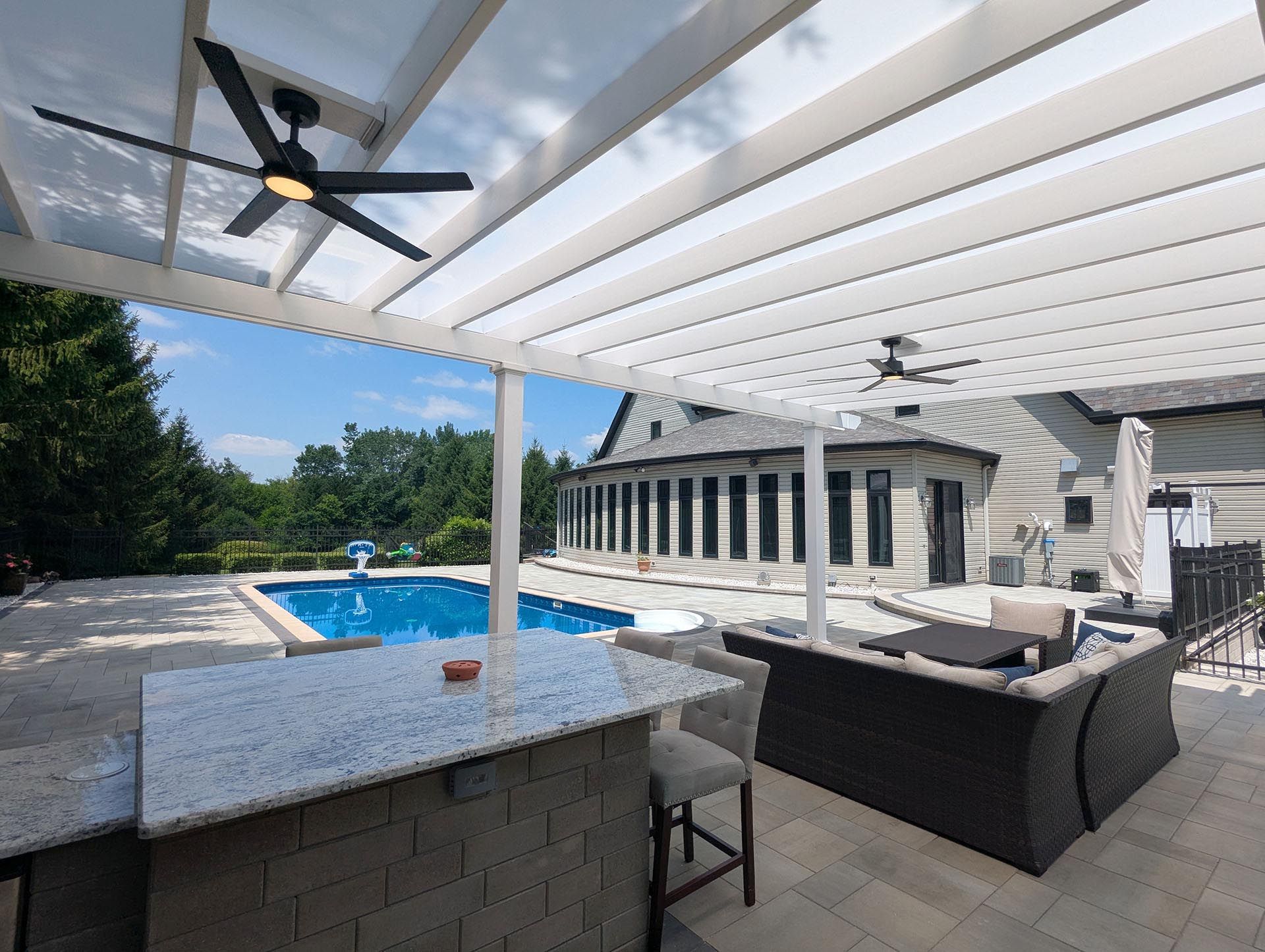 A covered outdoor patio featuring a granite bar, seating area, and swimming pool