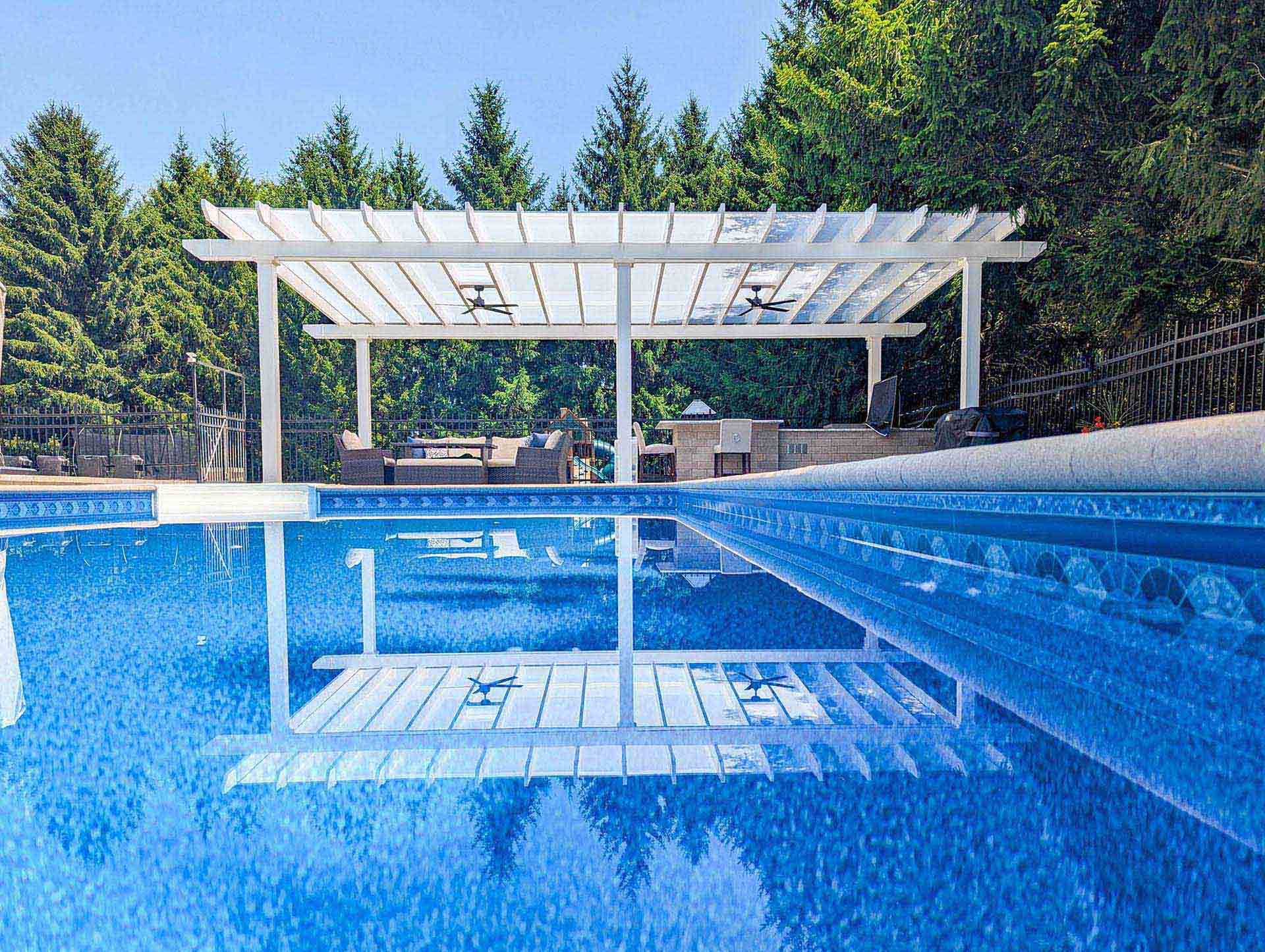 A bright, modern white pergola shades a patio area beside a vibrant blue swimming pool
