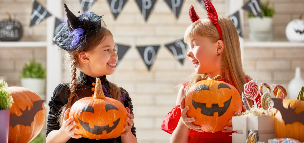 Two kids smile at each other while carving pumpkins for halloween