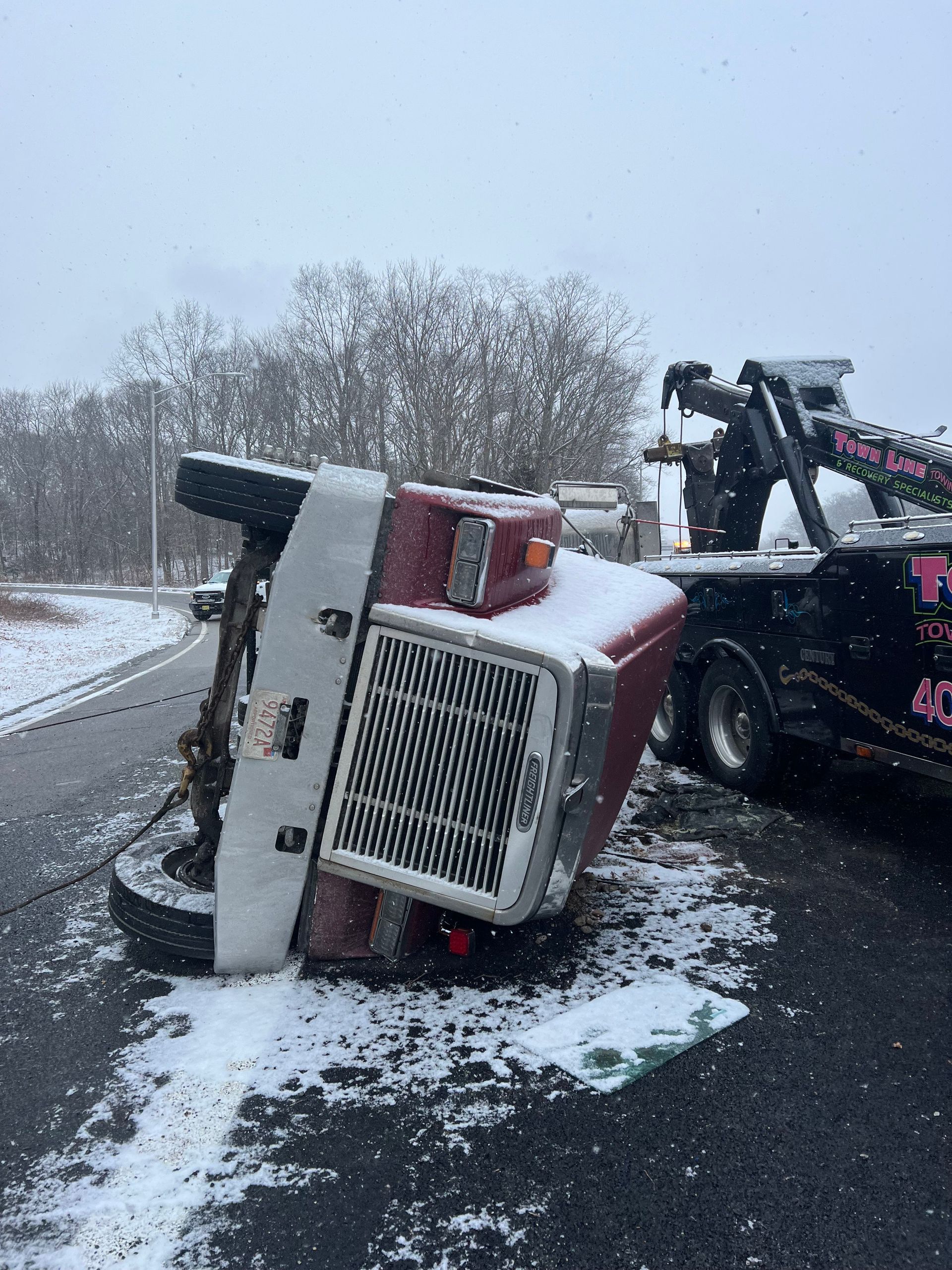A red truck is turned over on its side on the side of the road.
