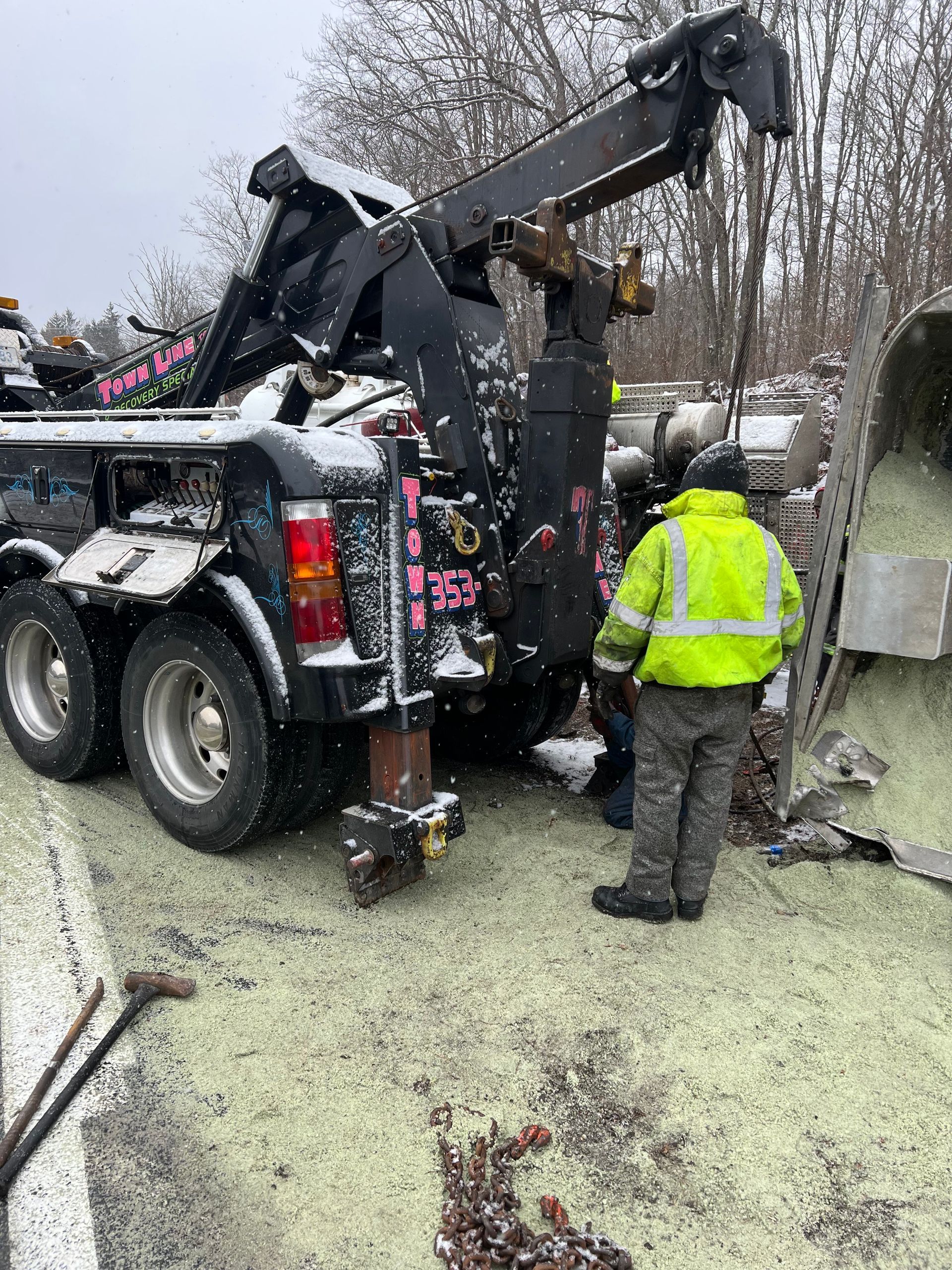 A man in a yellow jacket is standing next to a tow truck.