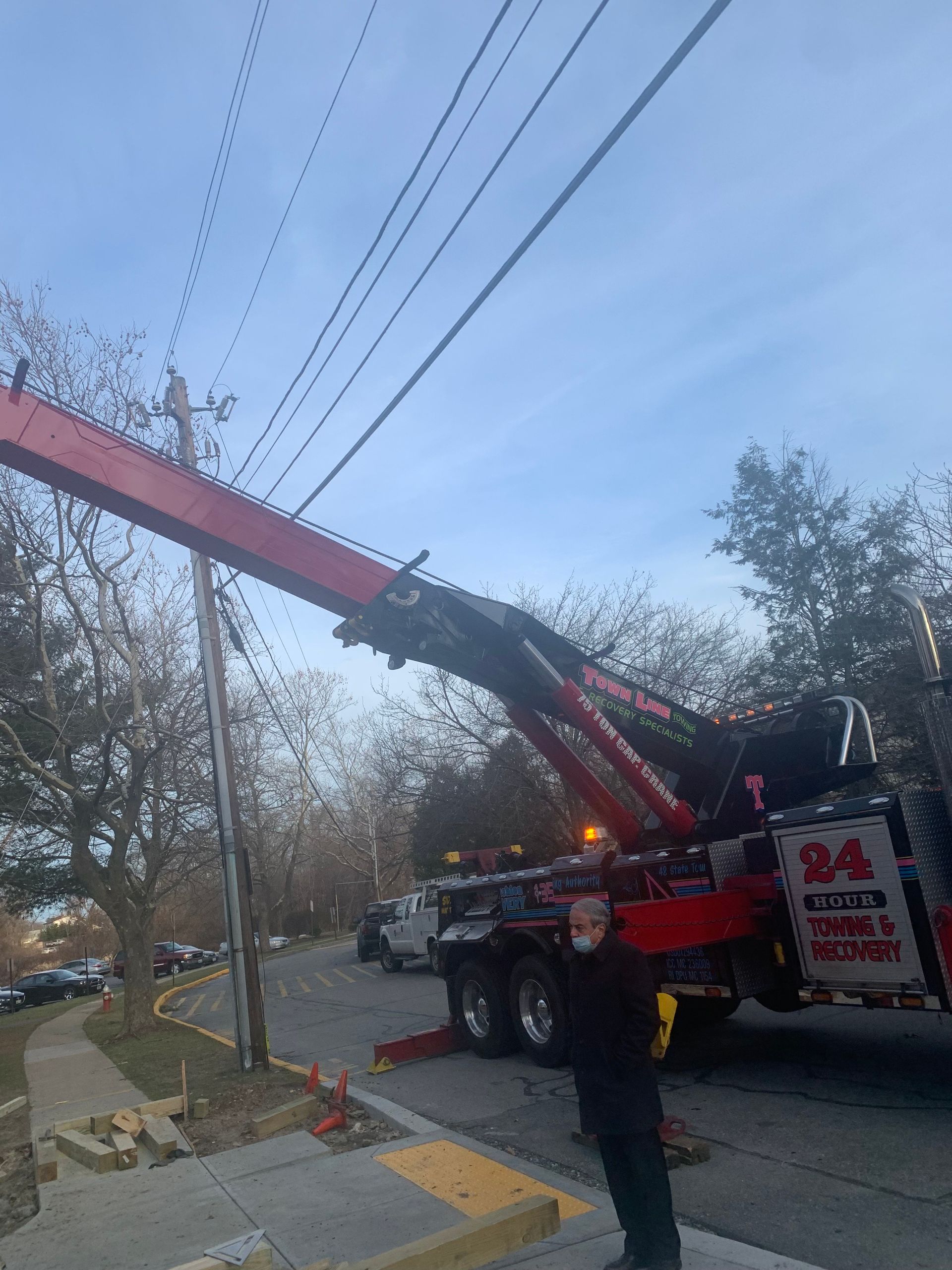 A man is standing next to a tow truck with a crane attached to it.