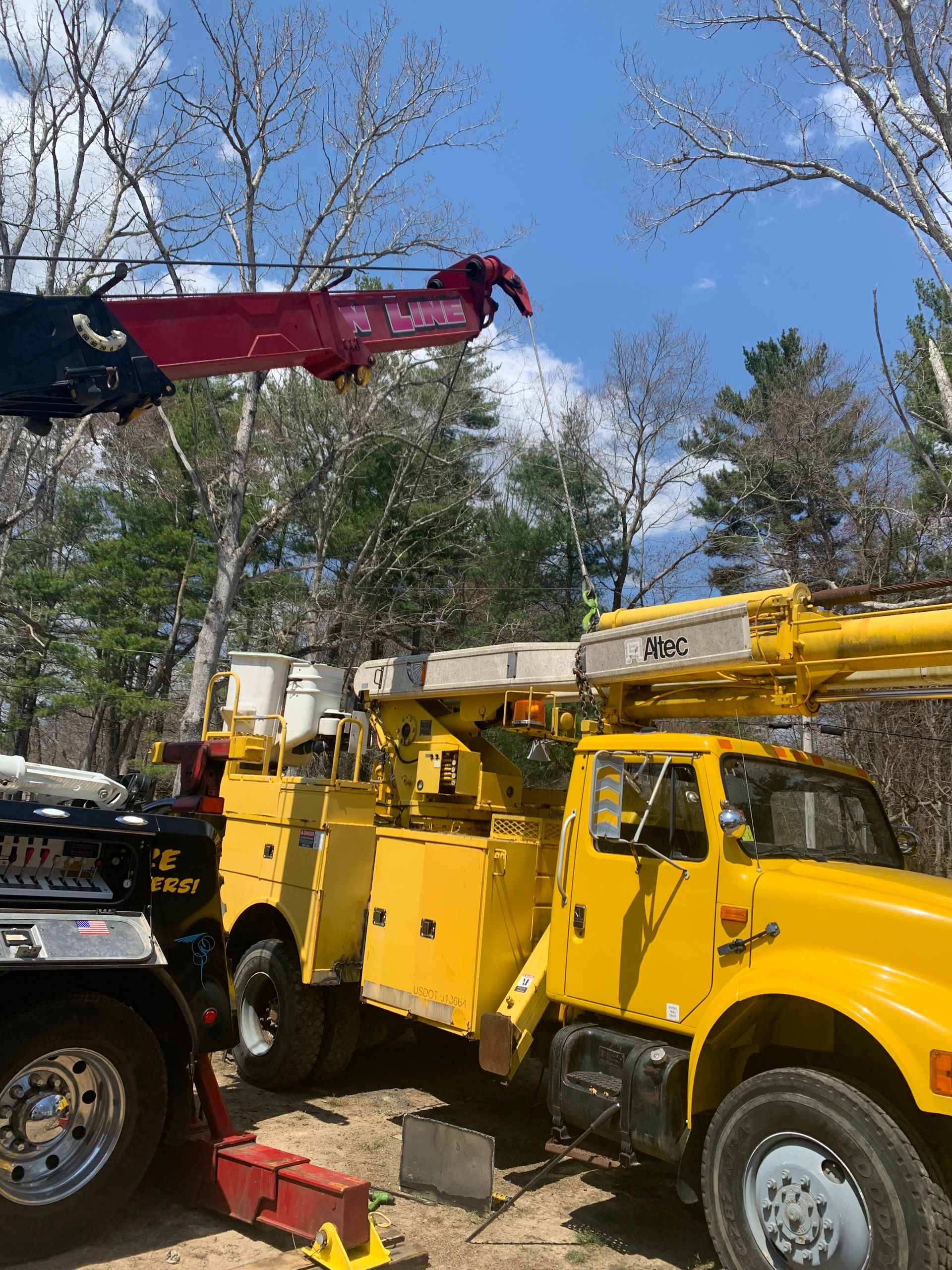 A yellow truck with a crane attached to it is parked next to a black truck.