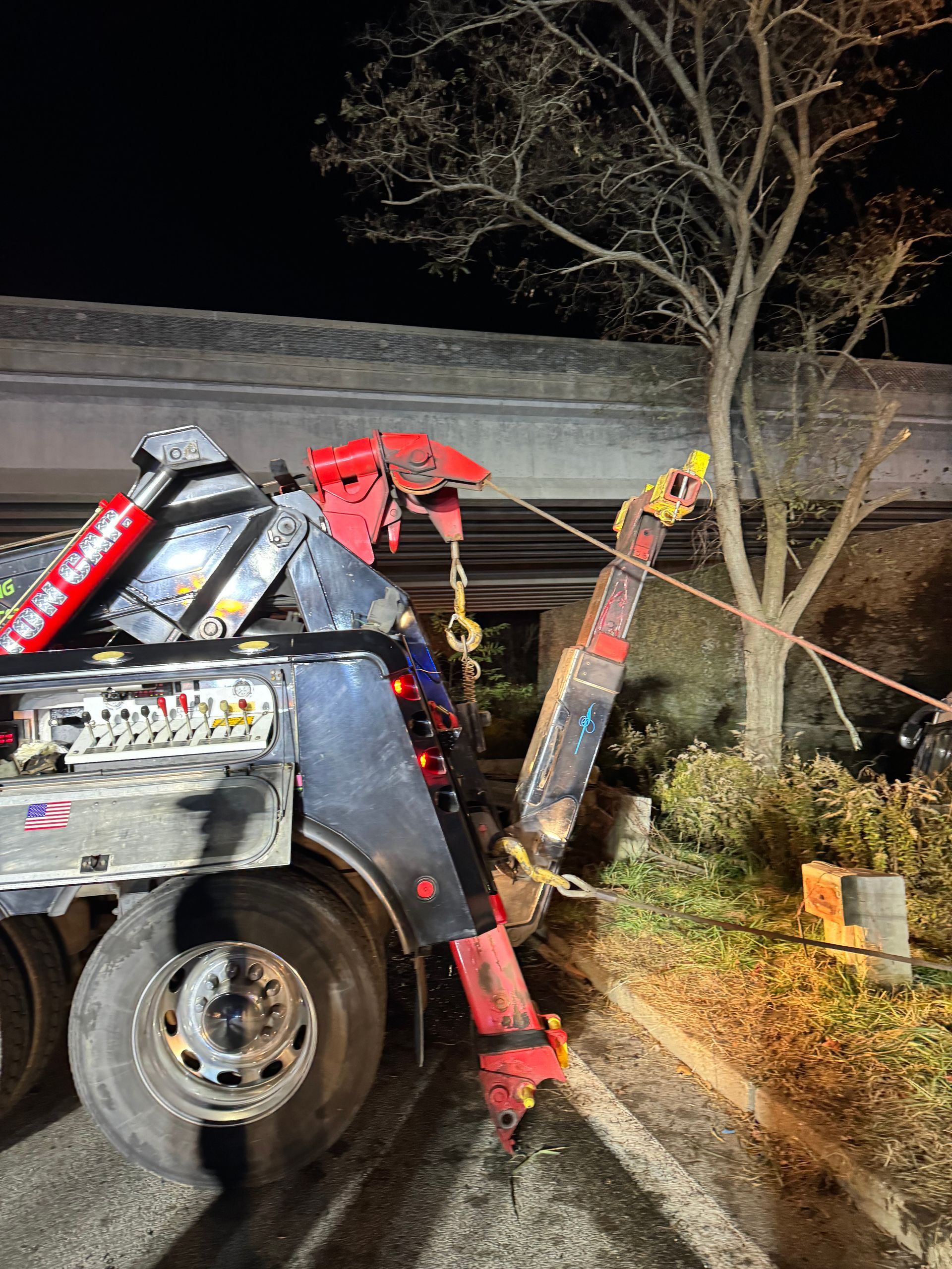 A tow truck is sitting on the side of the road next to a tree.