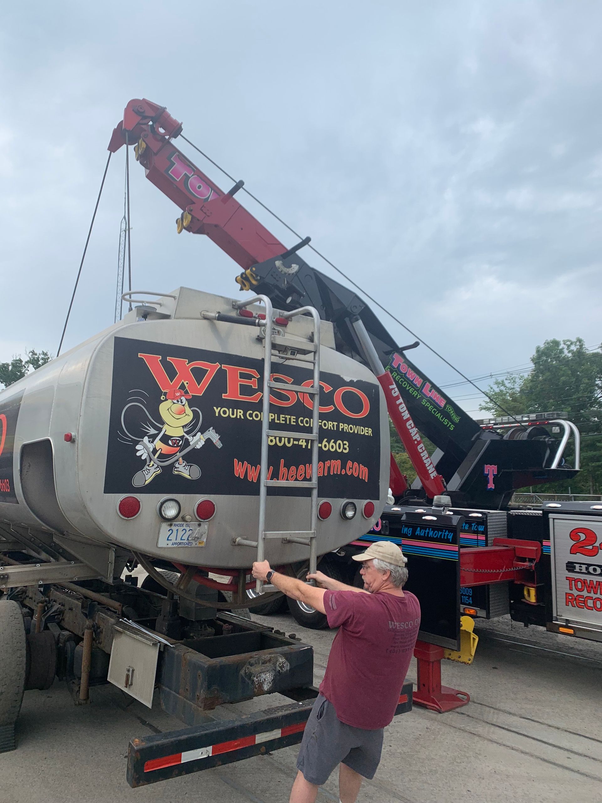 A man is standing next to a tanker truck with a crane attached to it.