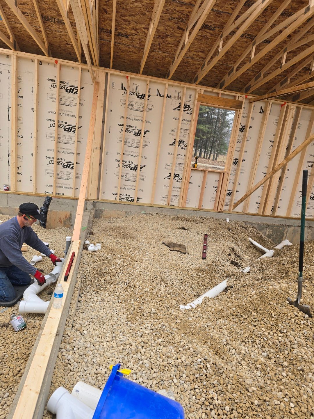 Worker installing flooring in an unfinished house interior with exposed framing.