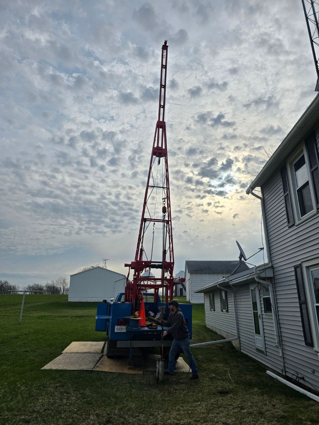 Worker beside red drilling rig near a house at dusk