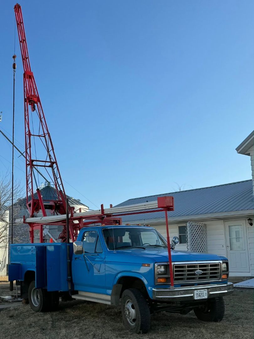 Blue drilling truck with red rig parked outside a building under a clear sky