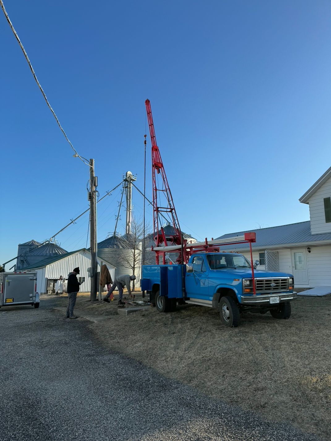 Blue utility truck and red crane at a worksite beside a building under a clear sky.