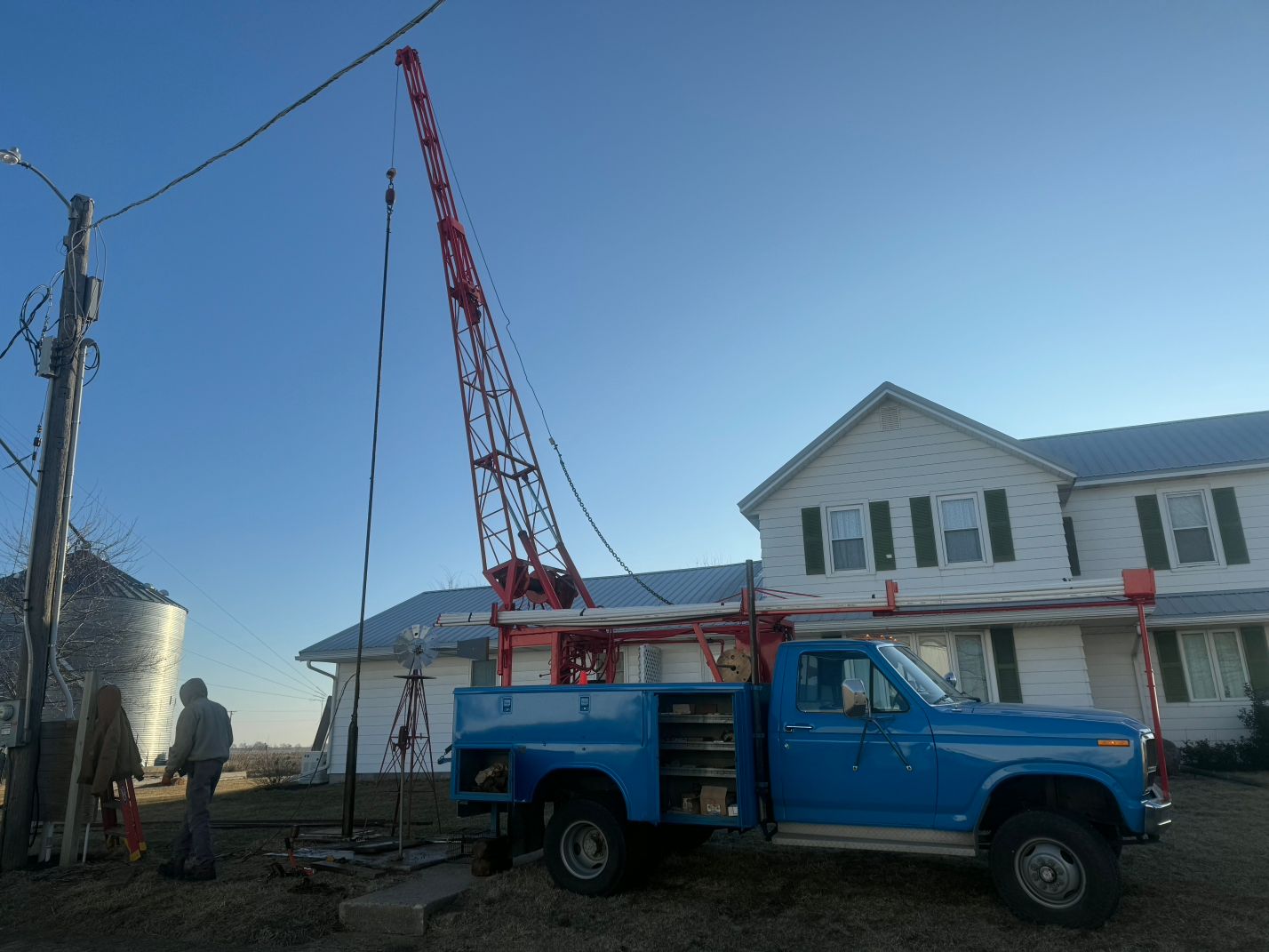 Blue utility truck with red crane parked beside a white house under construction
