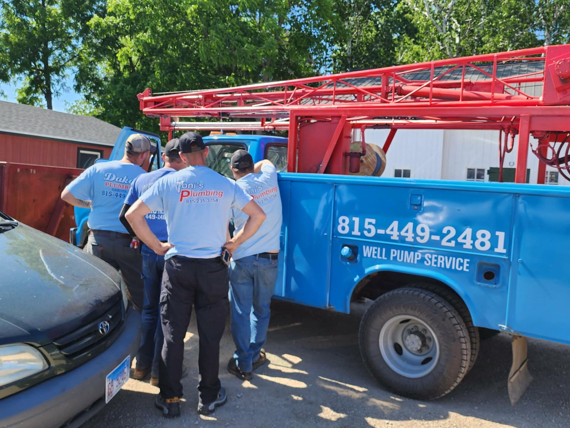 Workers gather by a blue well service truck with a red ladder rack beside a house.