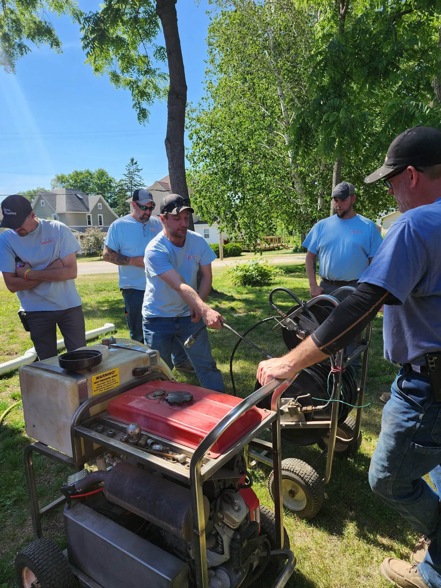 People gathered around a red generator outdoors, inspecting and discussing it in a sunny yard