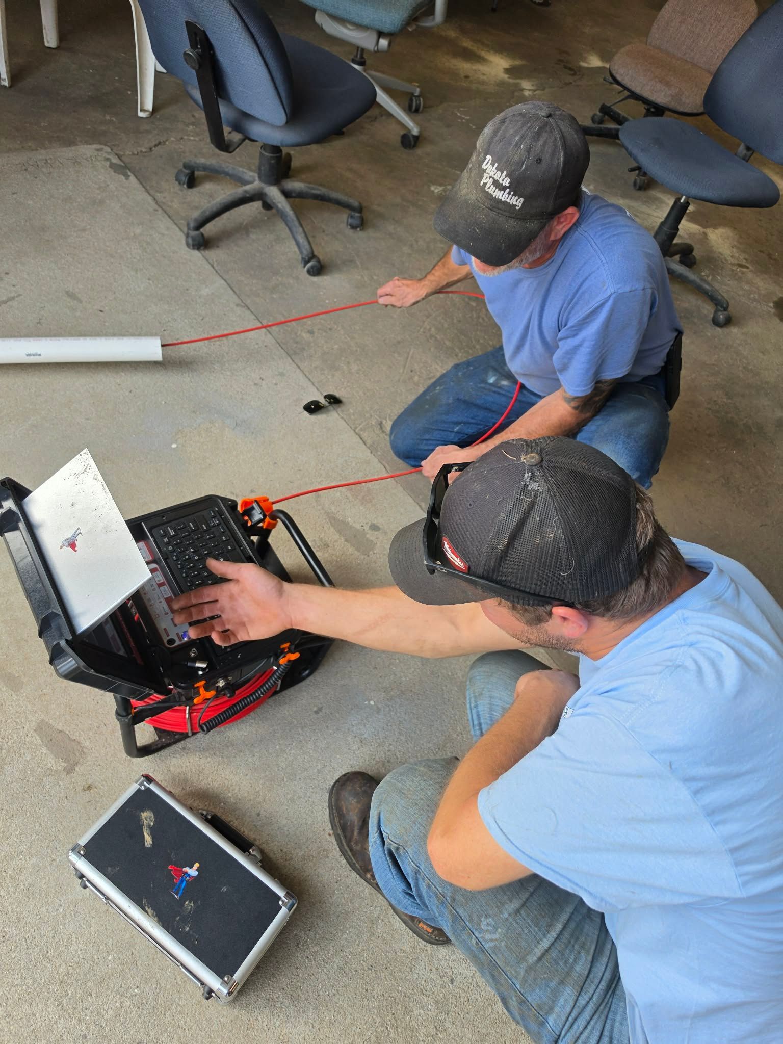 Two people working on a laptop and equipment on the floor in a classroom or workshop setting