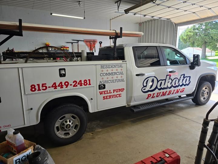 White Dakota Plumbing service truck parked in a garage, with red company lettering and phone number.