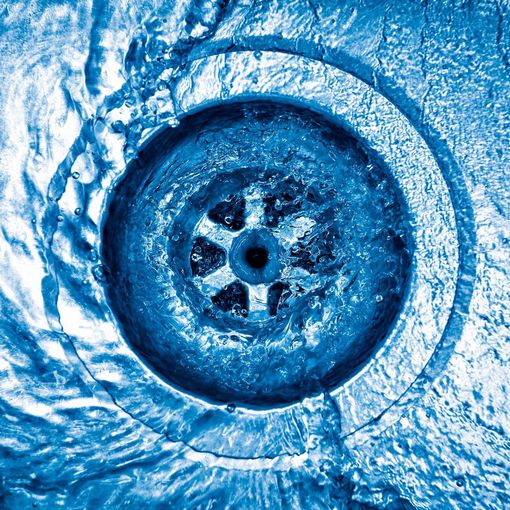 Close-up of a blue sink drain with a circular strainer and water ripples