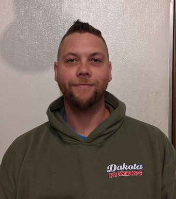 Man wearing an olive hoodie with a Dakota logo, standing against a light wall and looking at the camera