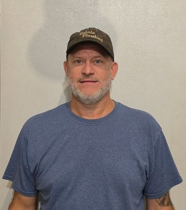 Man in a blue T-shirt and baseball cap standing against a plain wall.
