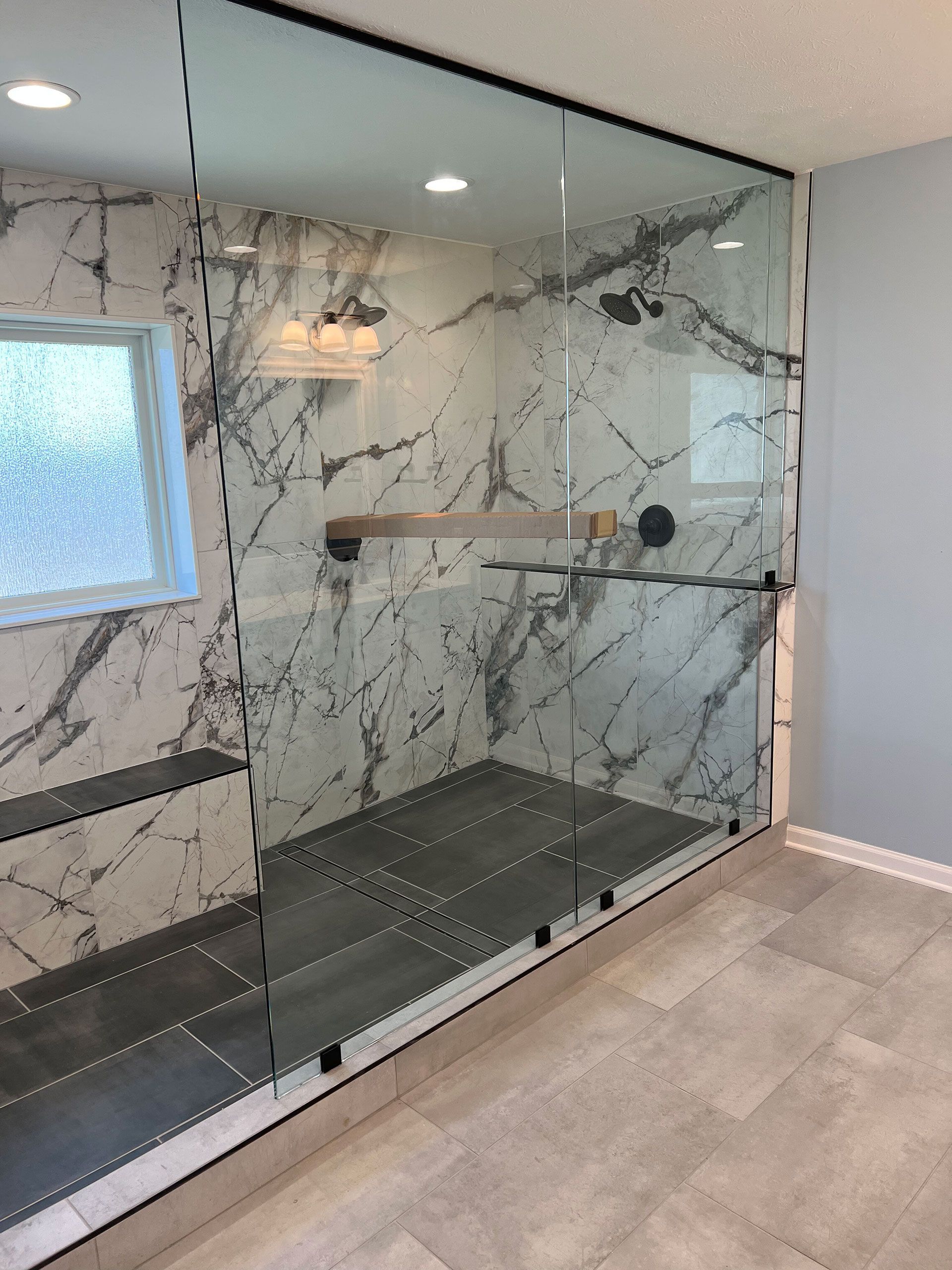 A bathroom with marble walls and a walk in shower with a glass door