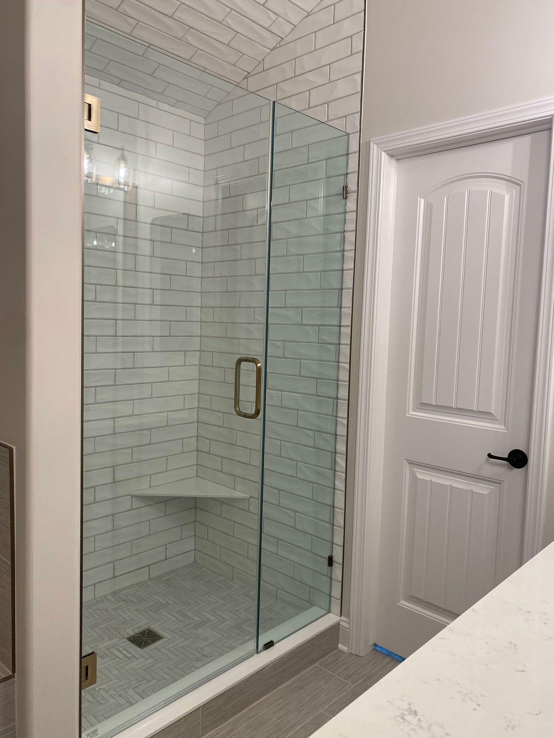 A bathroom with a glass shower door and white brick walls