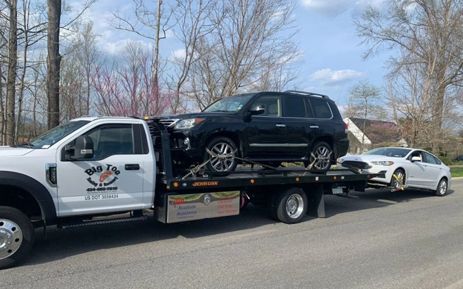 Tow truck with black SUV and white car loaded on its bed on a road.