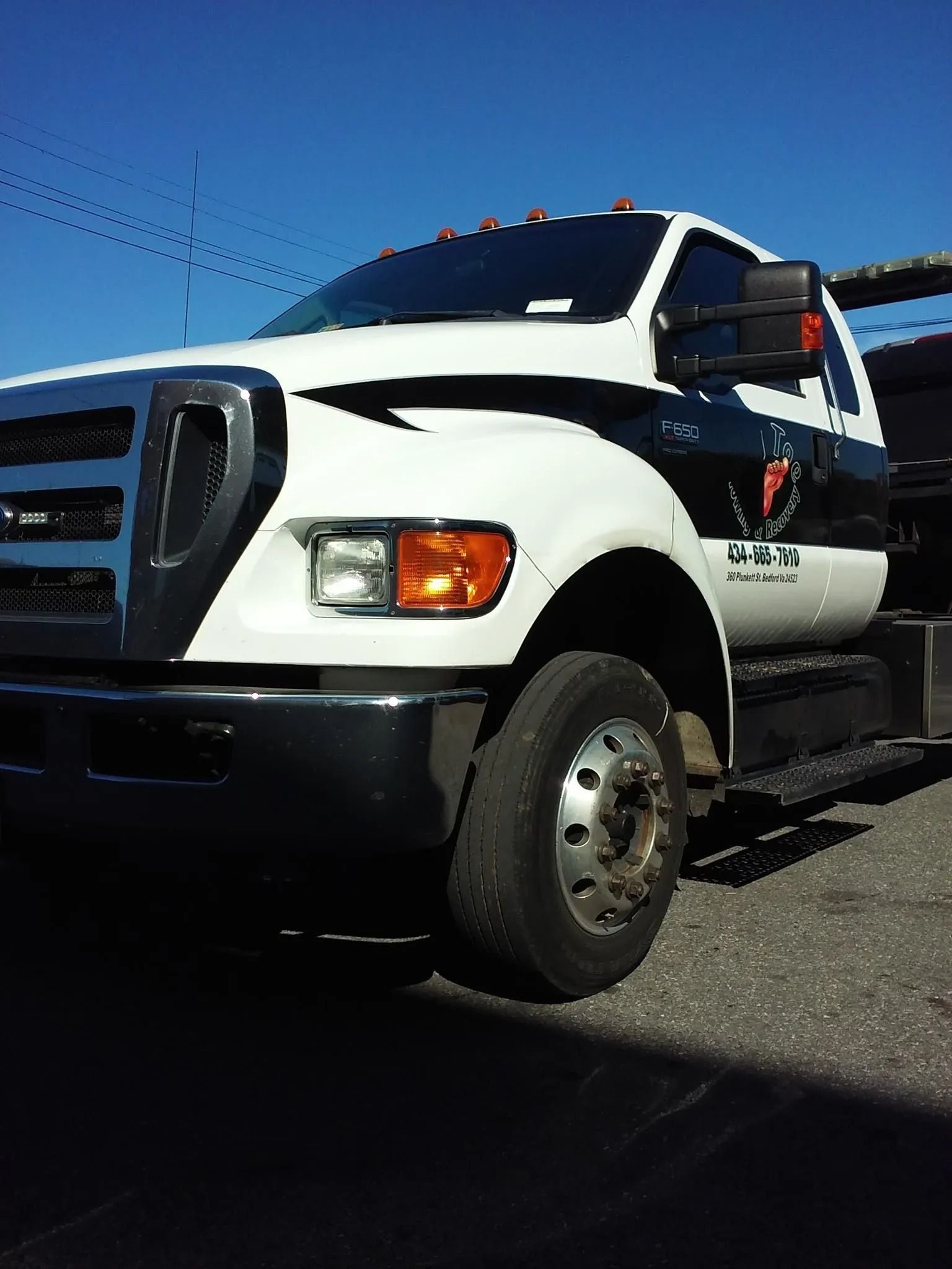 White tow truck with black accents parked on pavement under a blue sky.