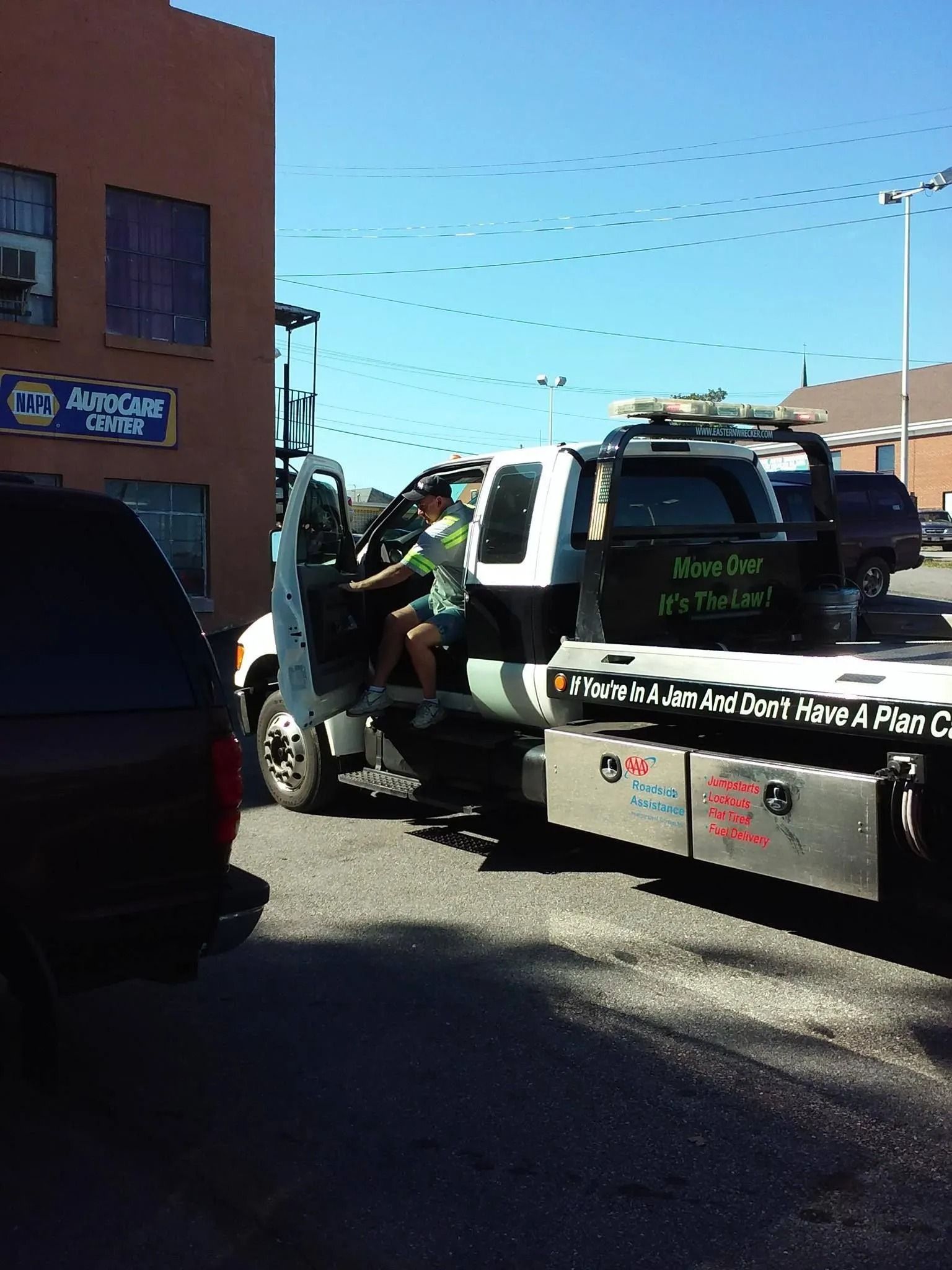 A person exiting a white tow truck parked next to a brick building on a sunny day.