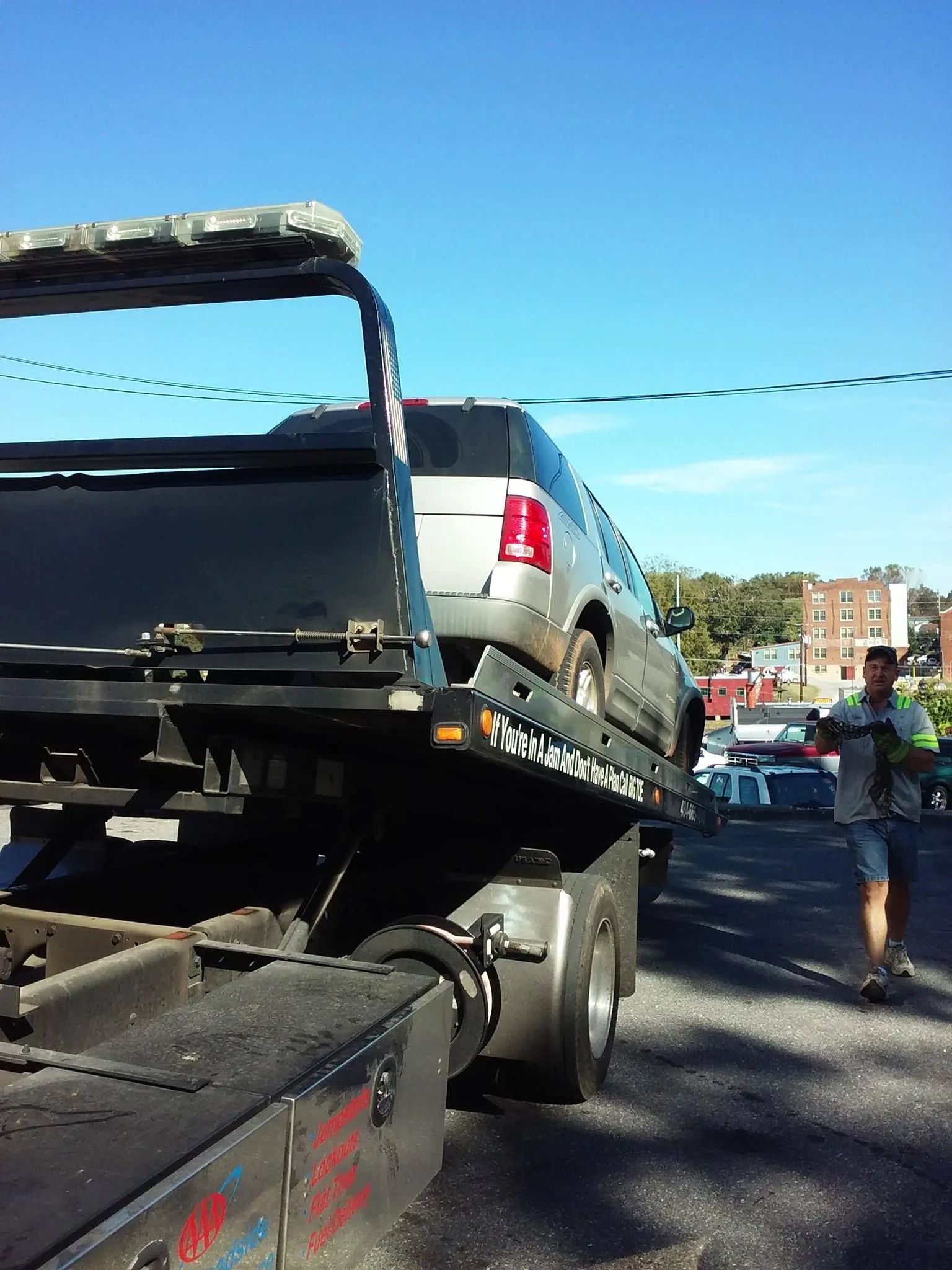 SUV being towed onto a flatbed tow truck on a sunny day. Man walking beside the truck.