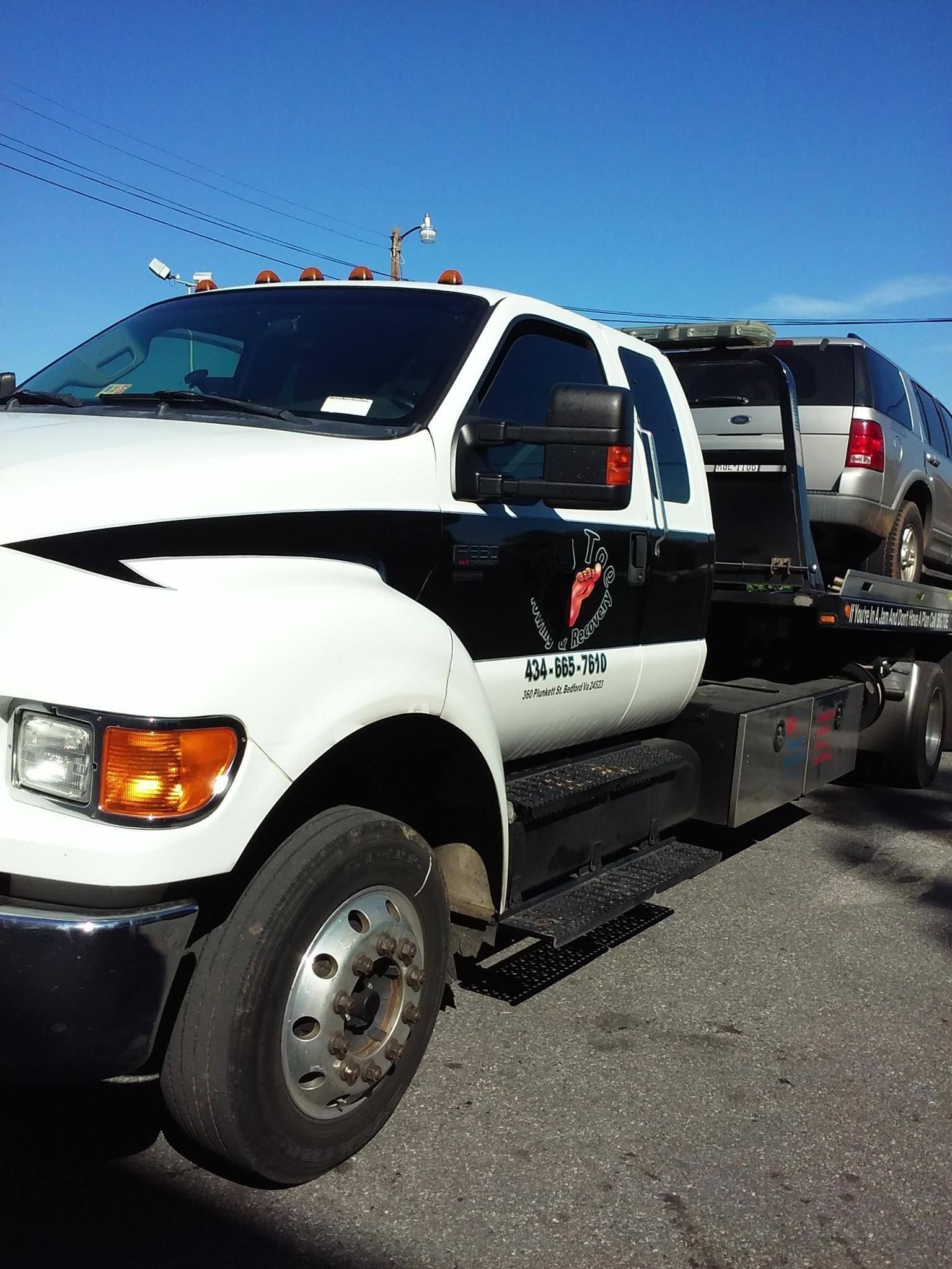 White and black tow truck with a car on its flatbed, under a blue sky.