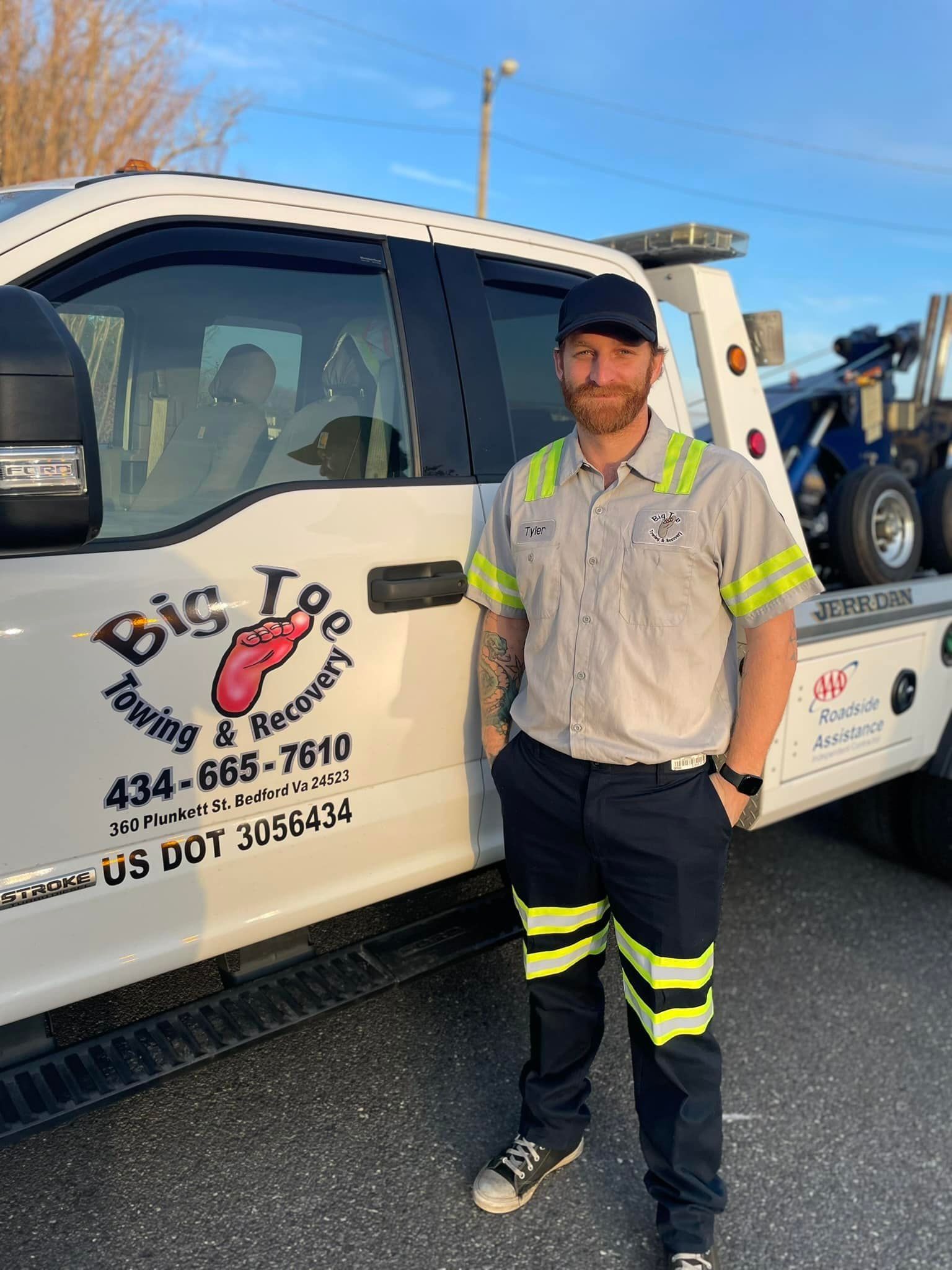 Tow truck driver standing by his truck, wearing a uniform. Truck has 