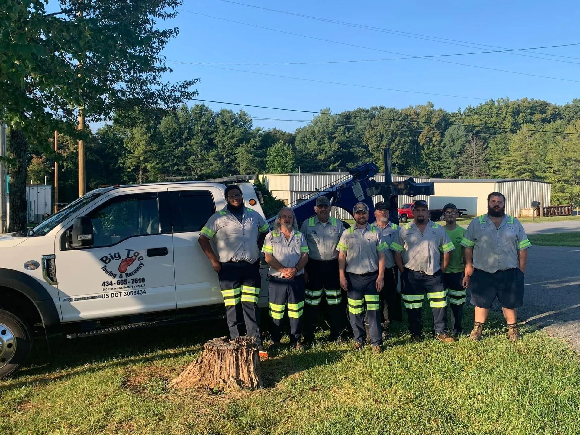 Group of people in uniform standing by a tow truck on a sunny day.