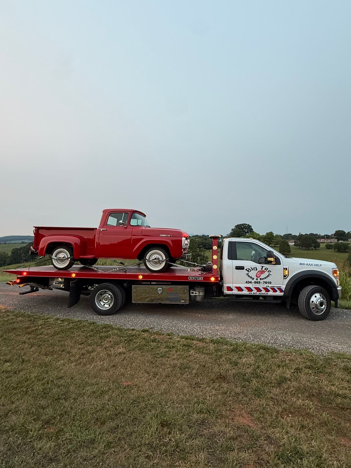 Red vintage pickup on a flatbed tow truck in a grassy field under a pale sky