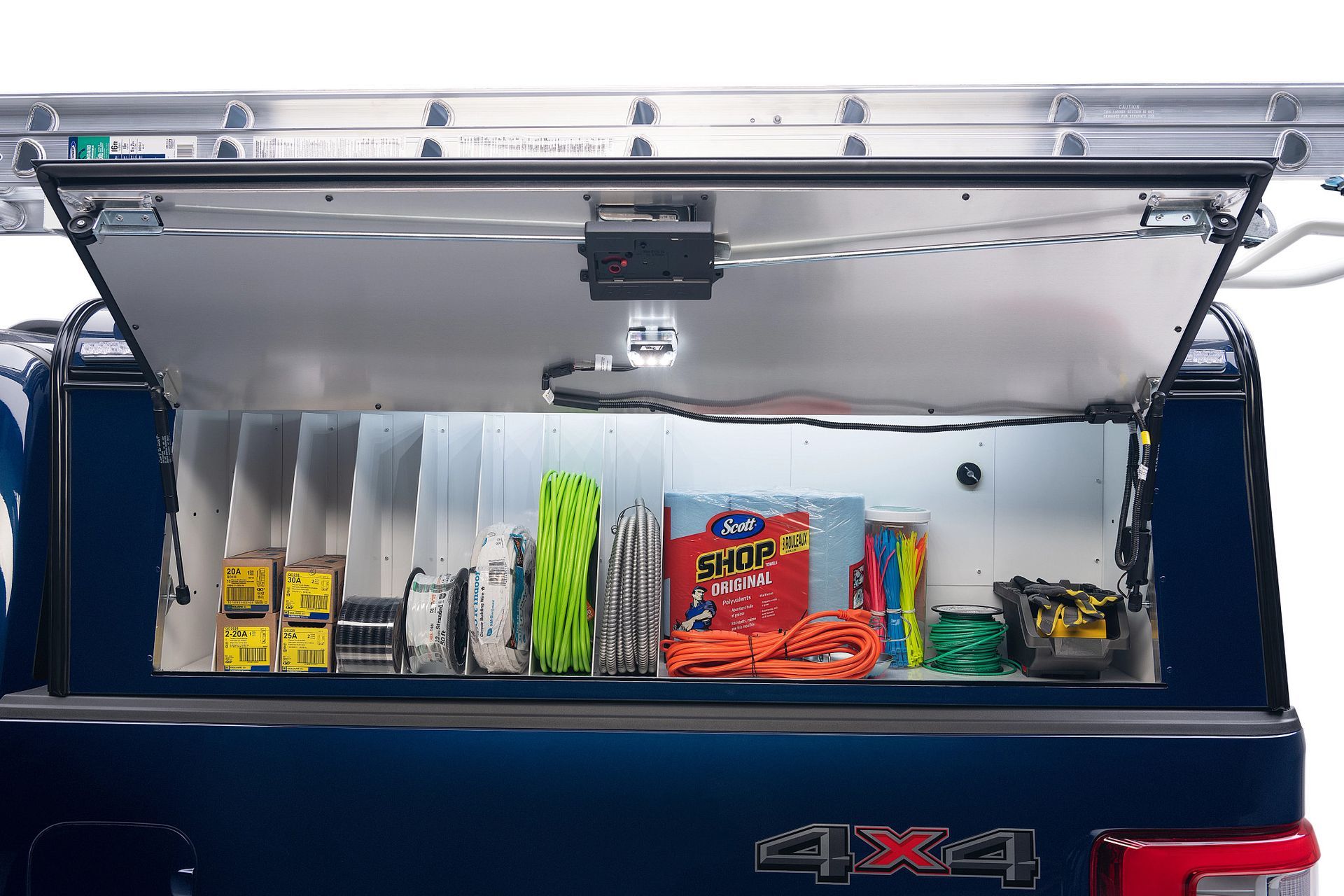 Open side storage compartment of a blue truck, containing organized tools, ropes, and supplies with an interior light.