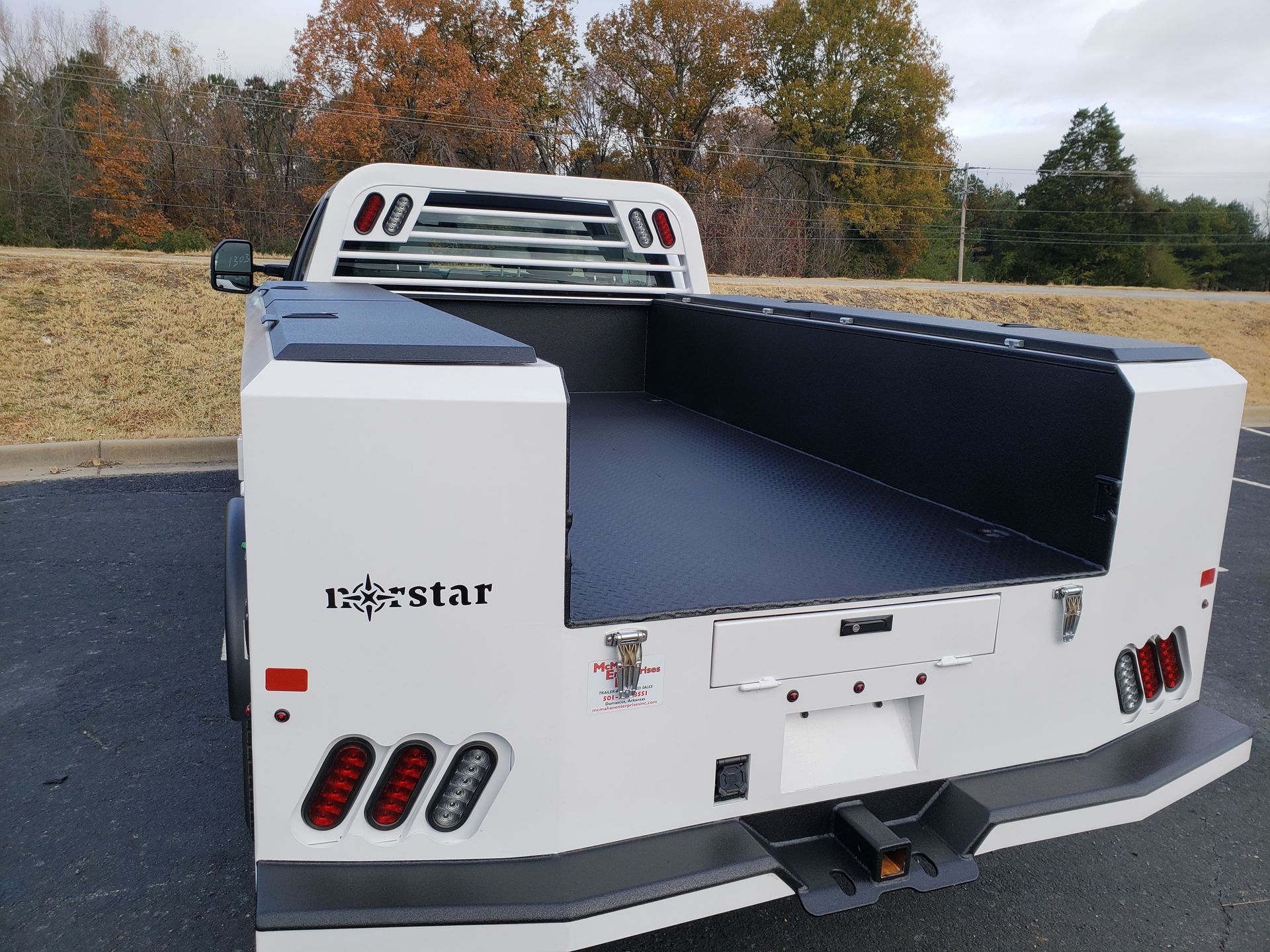 The rear view of a white truck bed with black interior lining, a headache rack, and LED tail lights in a paved lot.