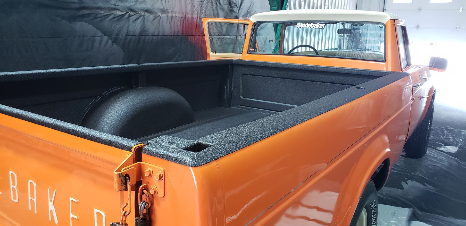 Bright orange pickup truck parked indoors with a black bed liner visible.