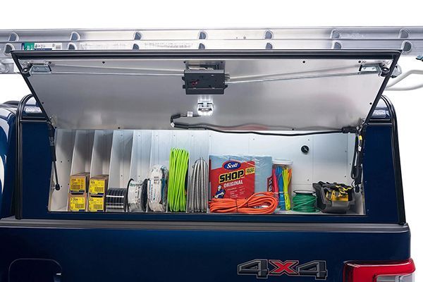 Open side compartment of a dark blue truck containing organized tools, supplies, and shop towels under an LED light.