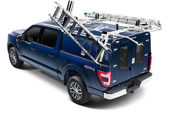 A blue pickup truck equipped with a specialized ladder rack system holding a ladder on its roof and side.