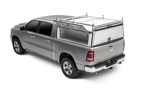 Silver pickup truck with a white utility topper and roof rack, showing the passenger-side door open.