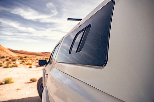 A close-up, angled view of a white truck topper window in a sunny desert landscape.