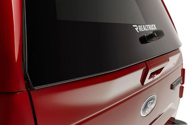 Close-up of a red truck tailgate featuring a RealTruck logo on the rear window and a Ford emblem below the handle.