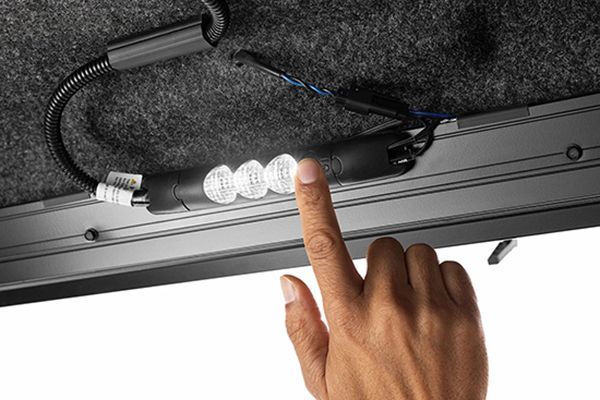 A hand presses a button on a small, illuminated LED light strip mounted to the interior of a vehicle or trunk.