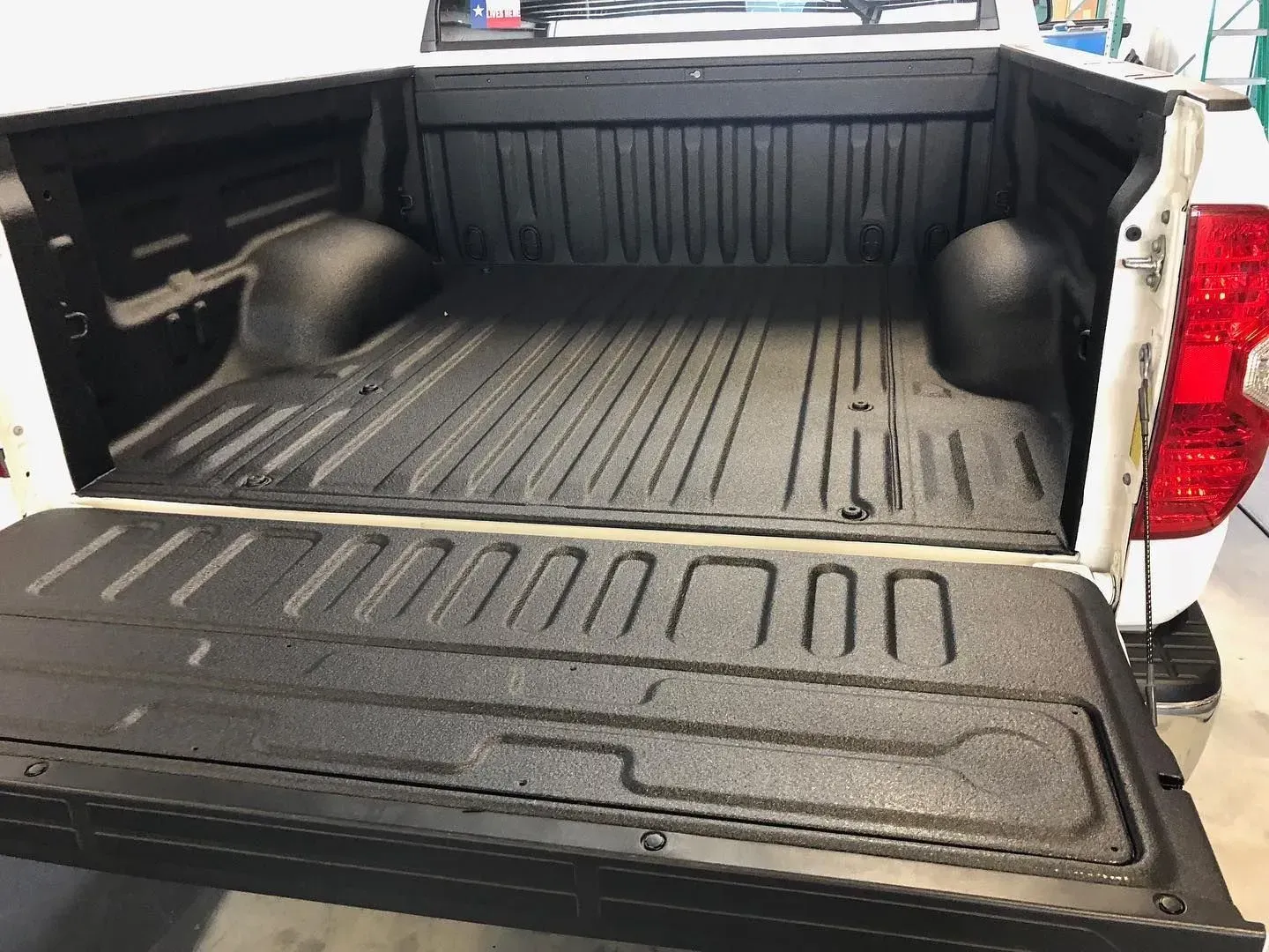 White truck bed with black textured liner; tailgate open.