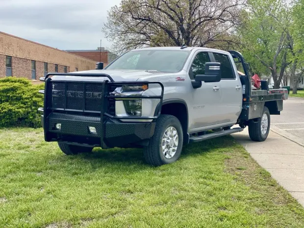 Silver work truck with a black bumper and flatbed parked on grass.