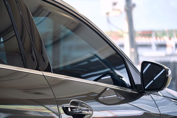 Dark-colored car with tinted windows and side mirror reflecting surroundings, parked outdoors.